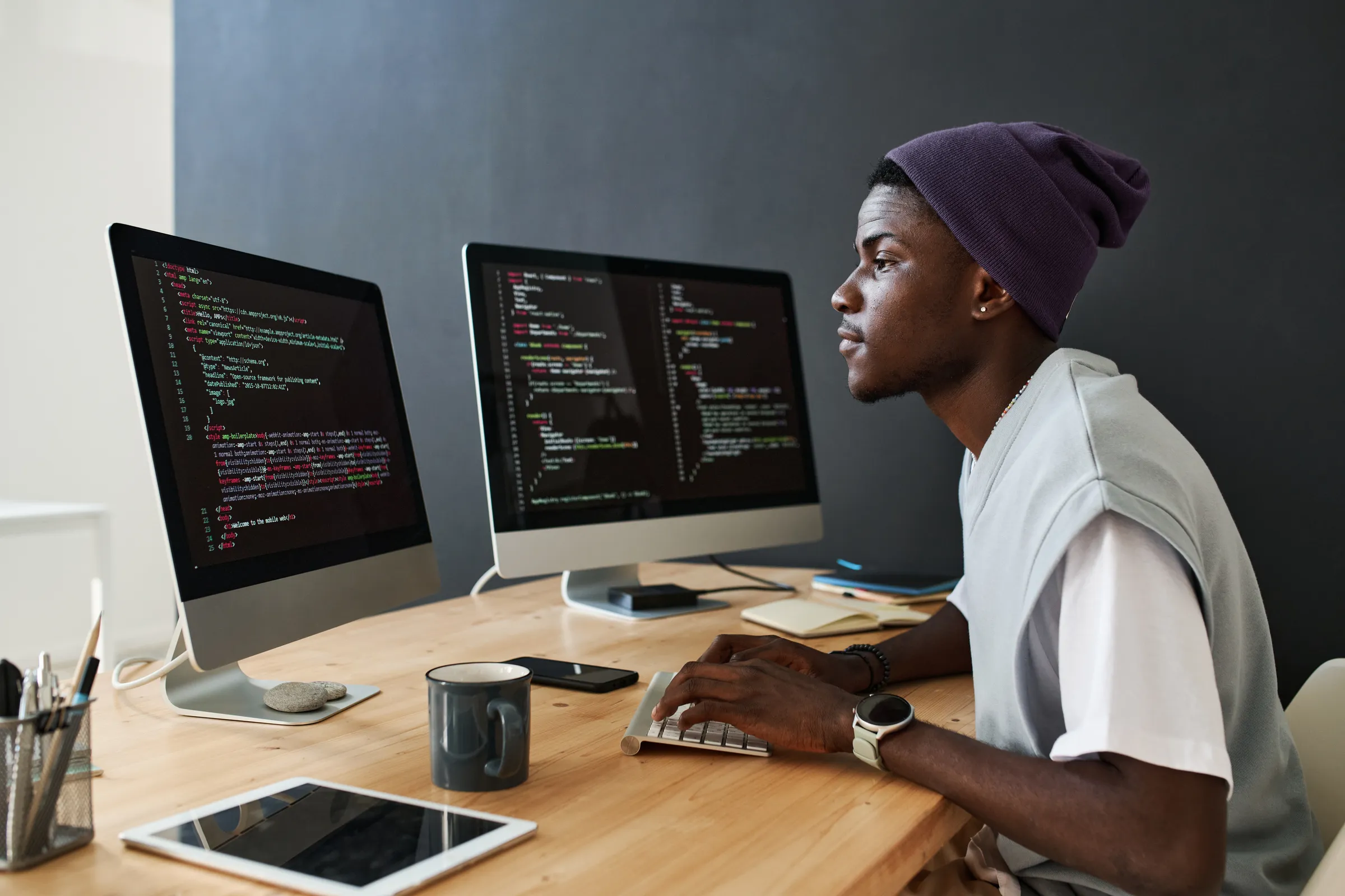 Jeune ingénieur développeur portant un bonnet, futur ingénieur en informatique, codant sur deux écrans dans un espace de travail lumineux.